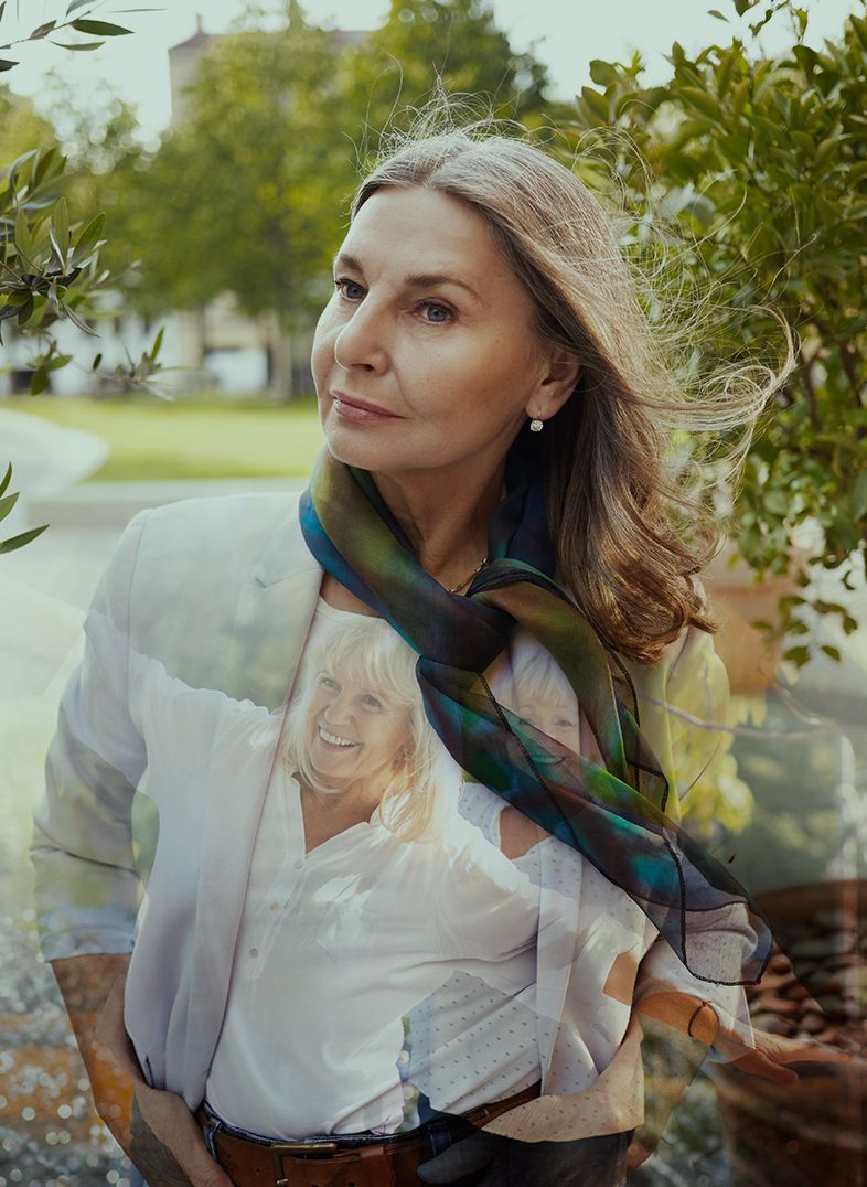 Woman in a white jacket and scarf looking to the side. A portrait of another woman is faintly visible on her shirt.