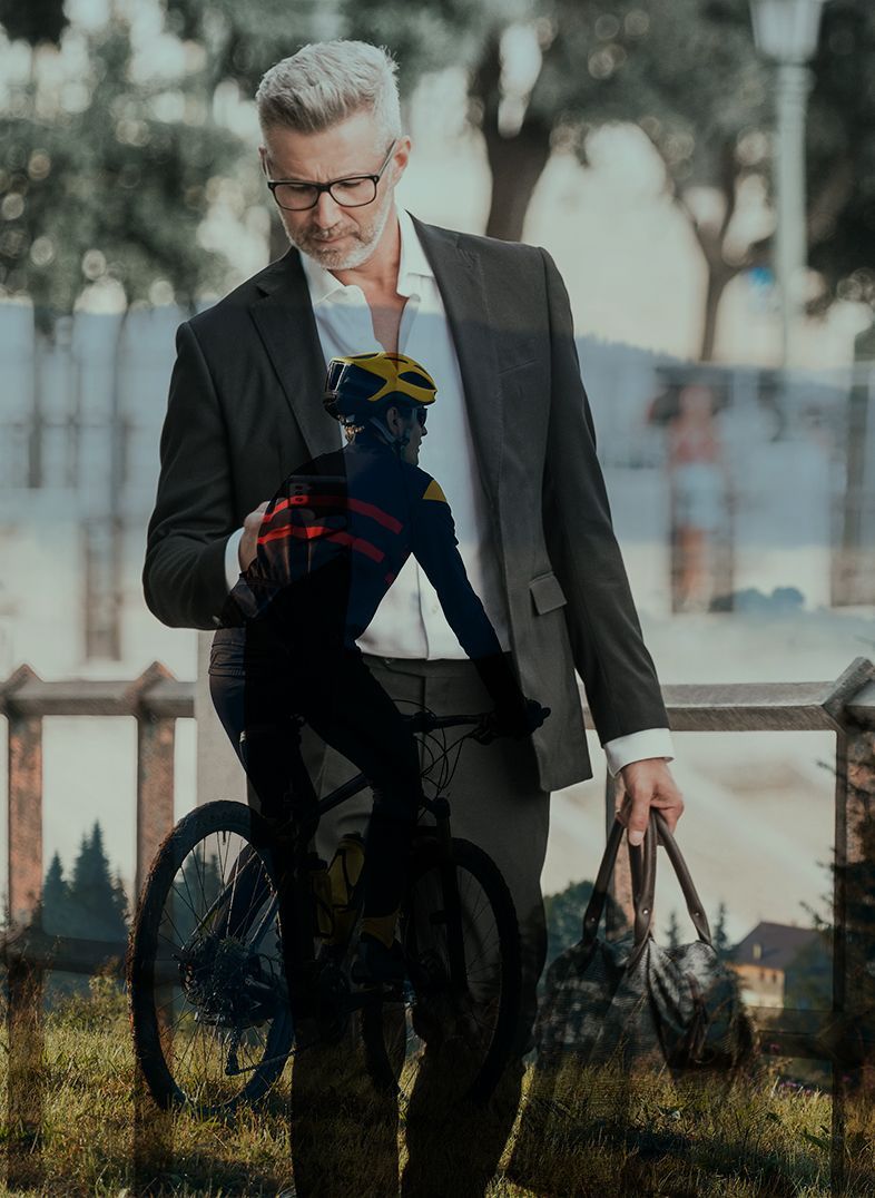 Man in suit, holding bike with cyclist; city background.