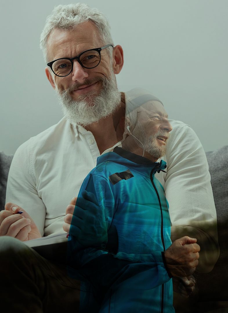 A man with a beard, wearing glasses, smiles. He has a superimposed image of himself outside wearing a blue jacket.