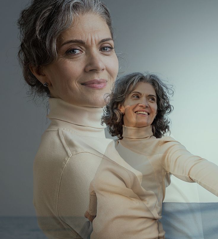 Woman with gray curly hair smiles, wearing a beige turtleneck, set against a blurred background.