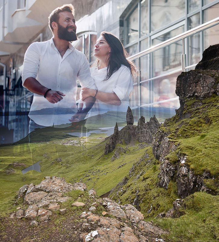 Couple in white, smiles and holds hands, superimposed over a green, rocky landscape.