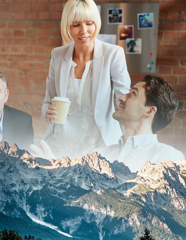 Business team with mountains superimposed; blonde woman holding coffee, talking to smiling man.