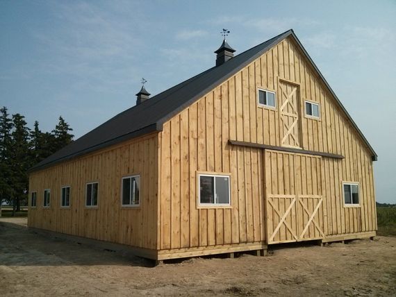 Wooden barn with black roof and open sliding door on a sunny day.