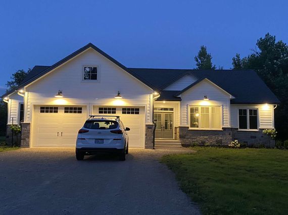 White house at dusk with lit garage, car in driveway, dark blue sky.