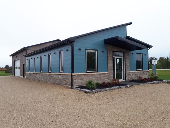 Modern building with blue and brick facade, windows, and a sloped roof, gravel driveway.
