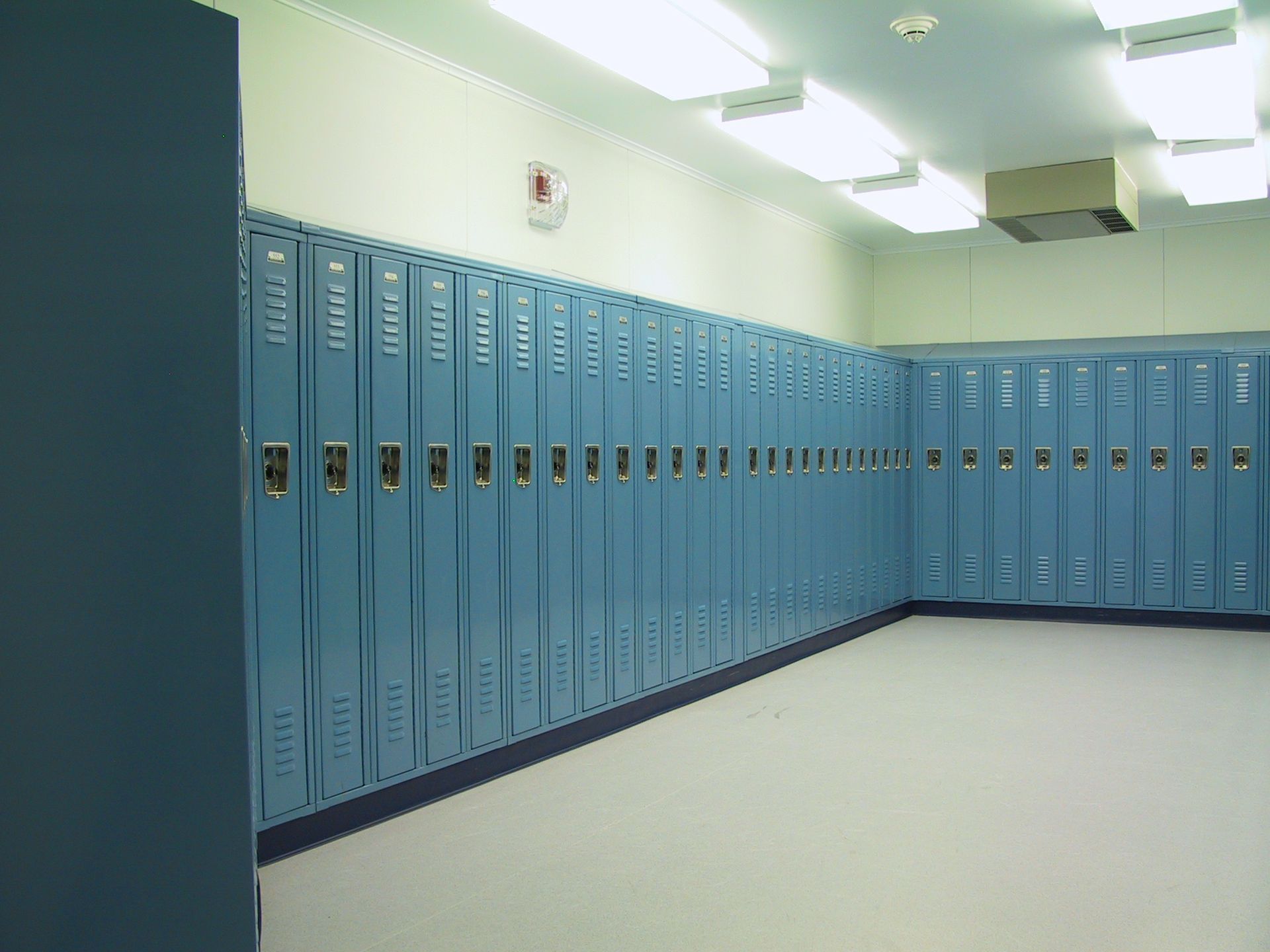 A row of blue lockers are lined up in a locker room.