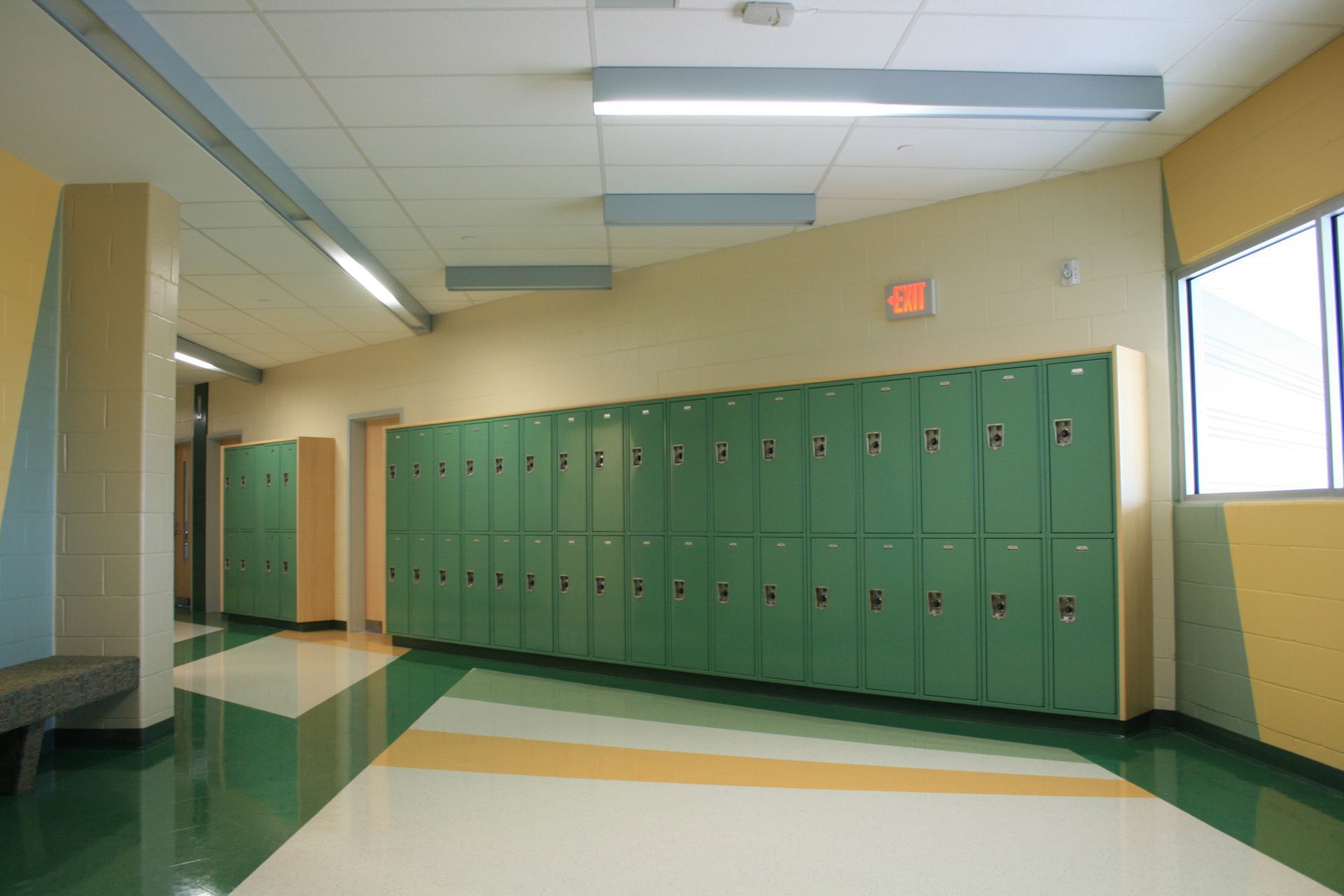 A hallway with green lockers and a red exit sign
