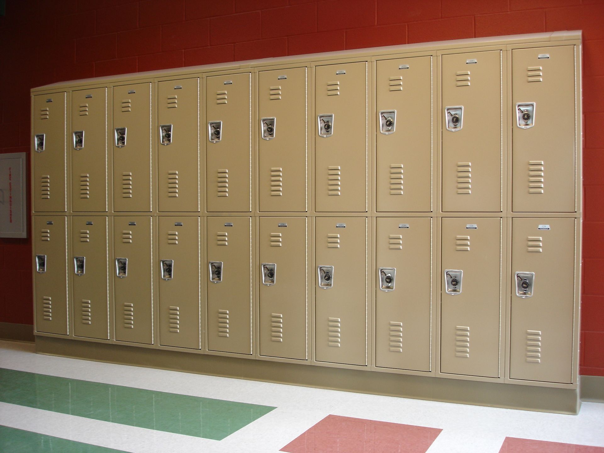 A row of tan lockers are lined up against a red wall