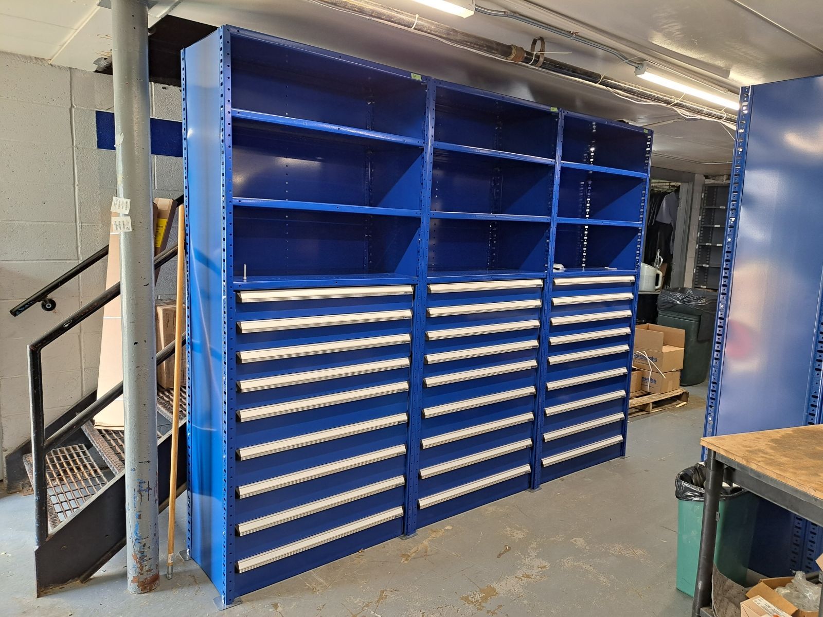 A warehouse with blue shelves and drawers and a staircase.