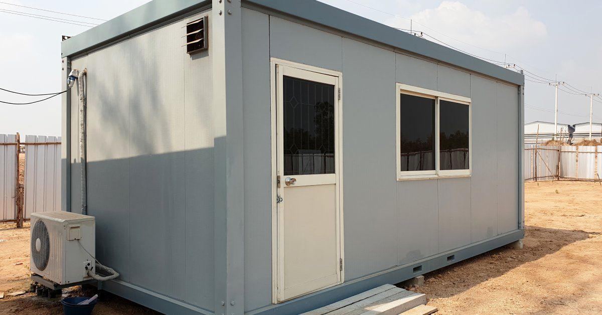 A light gray-colored modular modular office building sits outside in what appears to be a construction site.