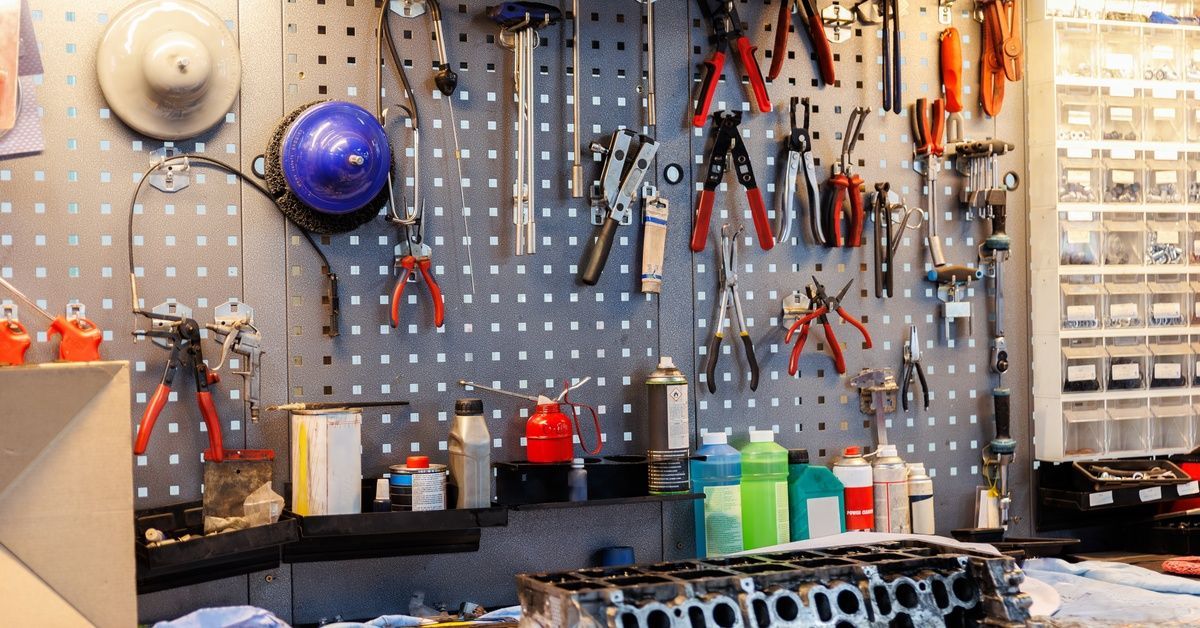 A close-up of a large pegboard with pliers, wrenches, and other tools hanging over a workbench in a workshop.