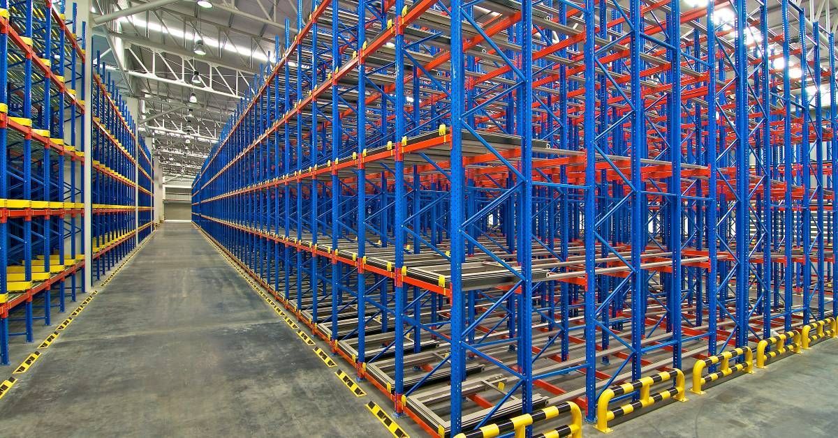 The interior of a large, empty warehouse with several rows of blue pallet racking systems lined up b