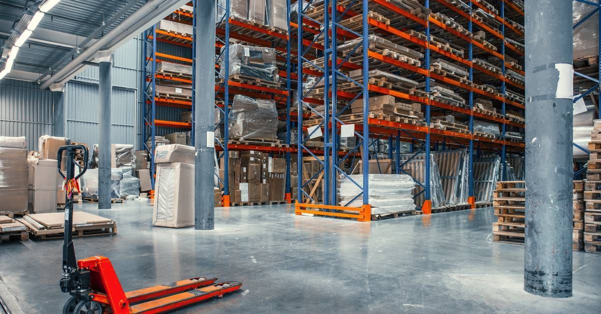 The interior of a warehouse is full of wooden pallets. A forklift is parked beside the pallet racks. 