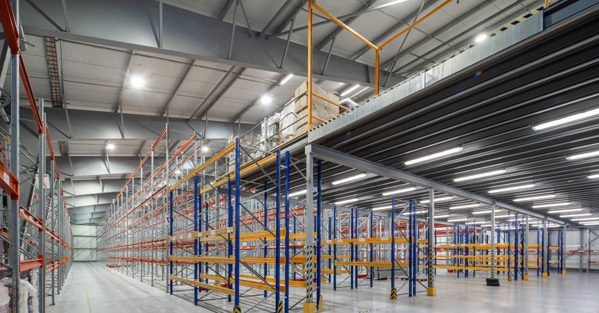  The interior of a well-lit, empty warehouse. There is a mezzanine built next to multiple pallet racks. 