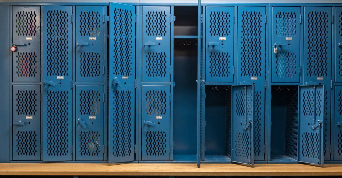 Blue metal cage lockers with open and closed doors in the locker room, accompanied by a wooden bench.