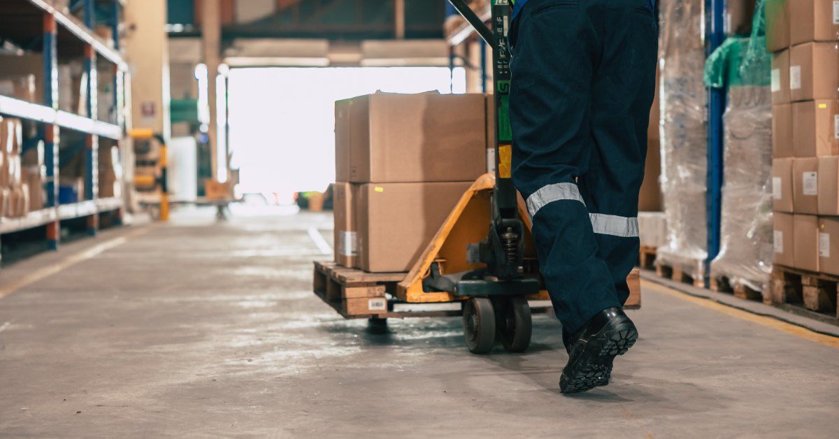 A person wearing a yellow high-visibility vest is pushing a stack of cardboard boxes towards an open door.