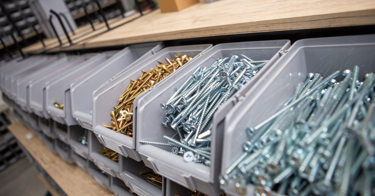 A row of screws in grey boxes with other boxes underneath them. The boxes are sitting next to a work table.