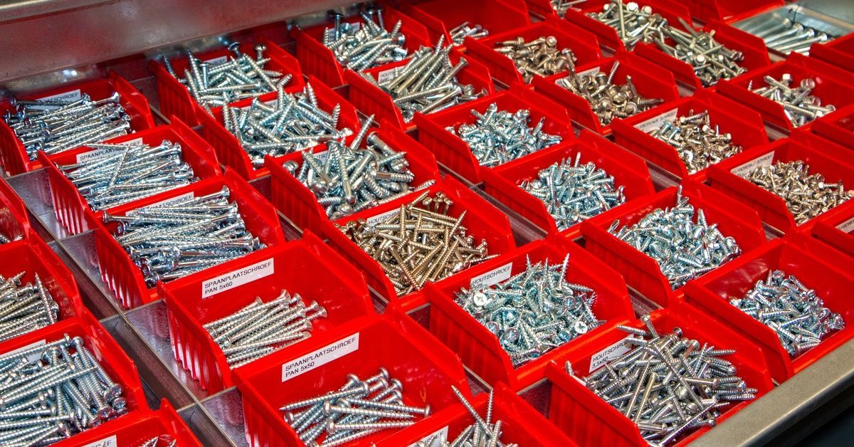 A large number of red trays with different-sized screws. Some of the screws are silver and others are copper.
