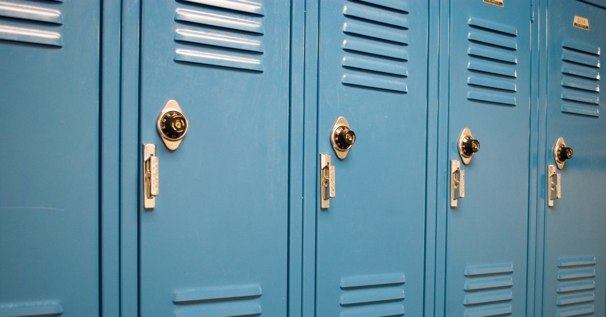 A row of blue lockers in a row together. They are all identical with locks and handles on the left side of the door.