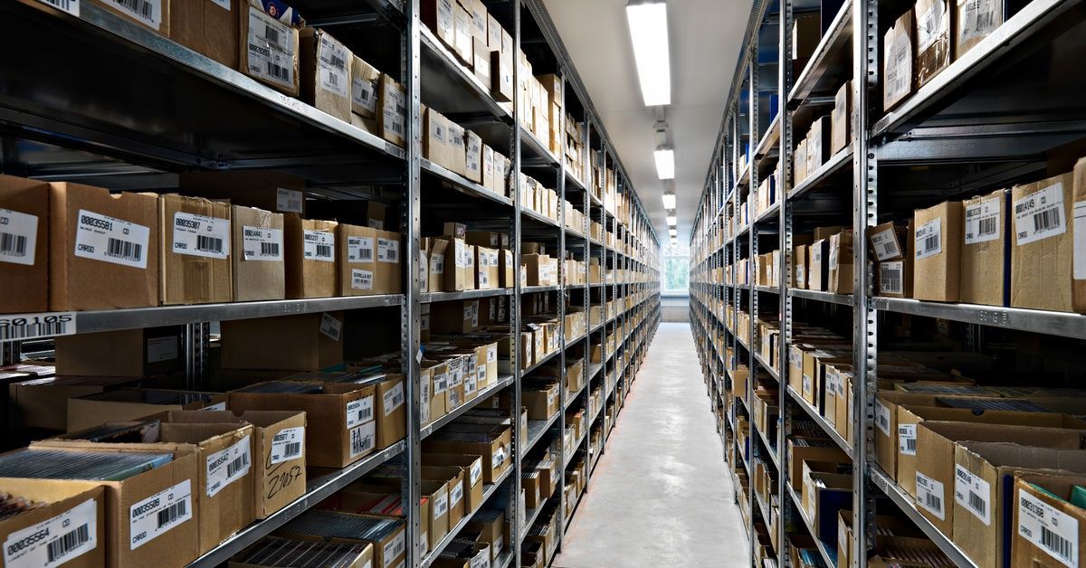 Rows of empty metal shelves in a storage room. Two of the shelves are against the wall, and the third is in the middle.
