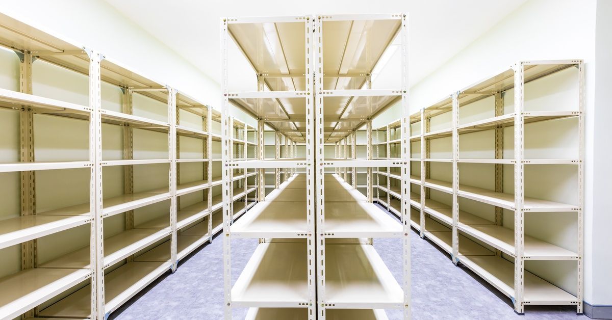 Rows of empty metal shelves in a storage room. Two of the shelves are against the wall, and the third is in the middle.