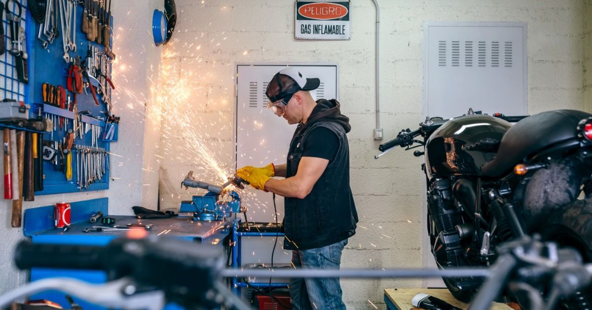 A mechanic is working with a grinder, and sparks are flying. He is in an automotive workshop with to