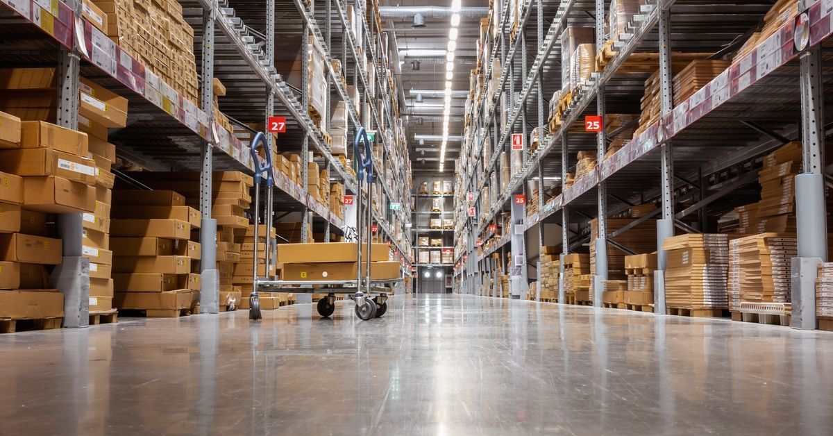 A row of tall shelves in a warehouse with no people in it. There is only a cart in the middle of the aisle.