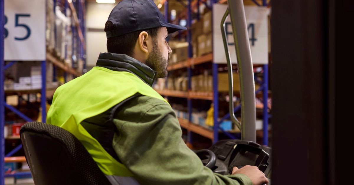 A forklift operator in a warehouse driving past large storage shelving.