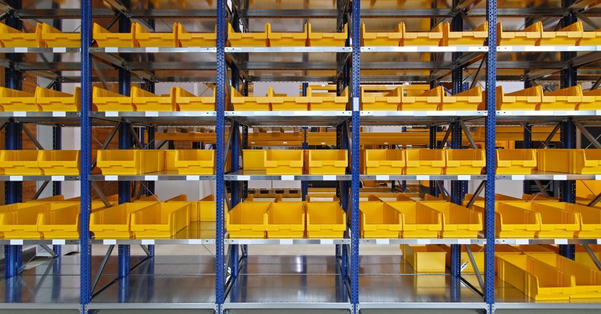 An empty warehouse with no products in it besides shelving units filled with small yellow bins.