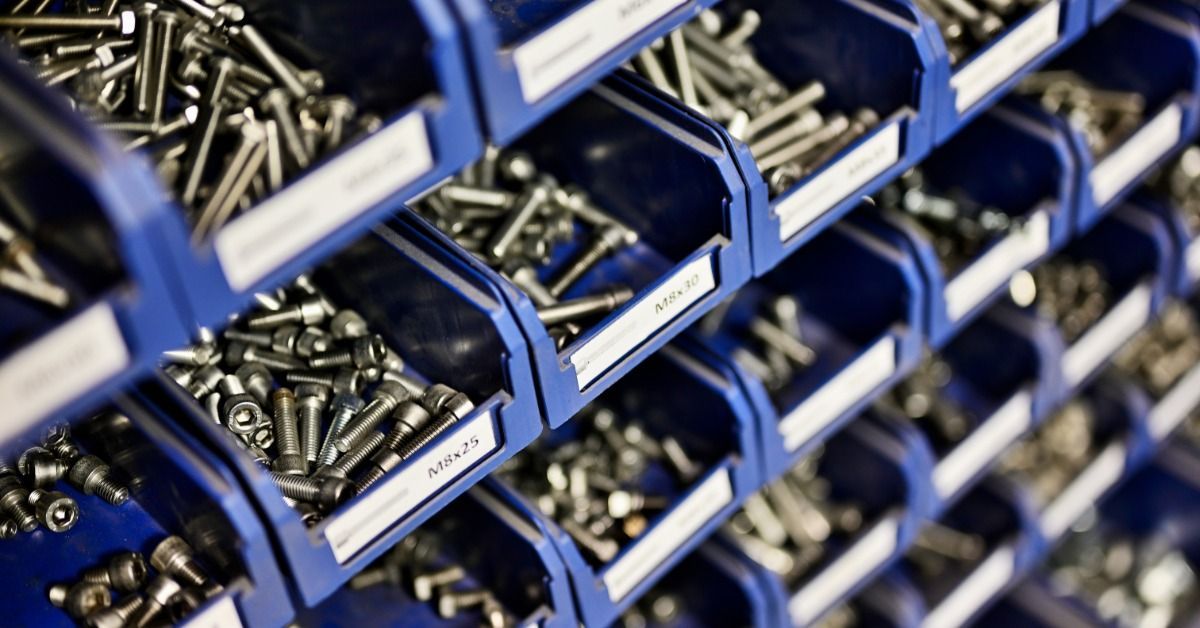 Multiple rows and stacks of small blue bins filled with metal materials such as nails, fasteners, and bolts.