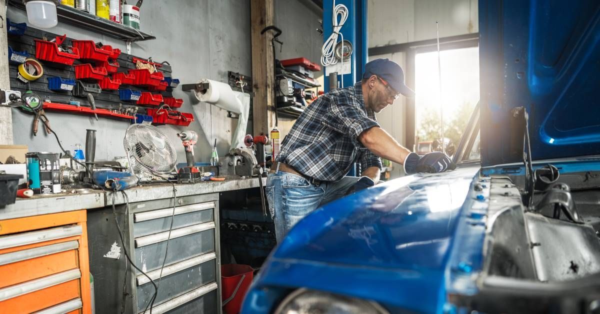 A mechanic working on a muscle car in his workshop. A large automotive workbench filled with tools l