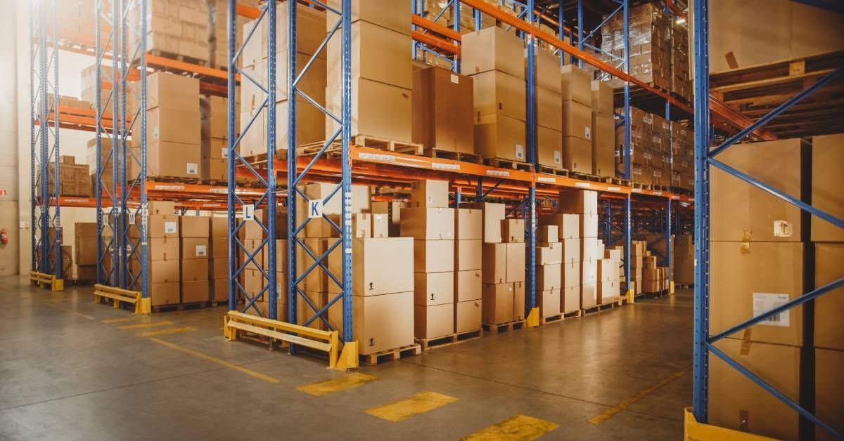 A modern retail warehouse featuring rows of metal pallet rack shelving systems full of stacked boxes