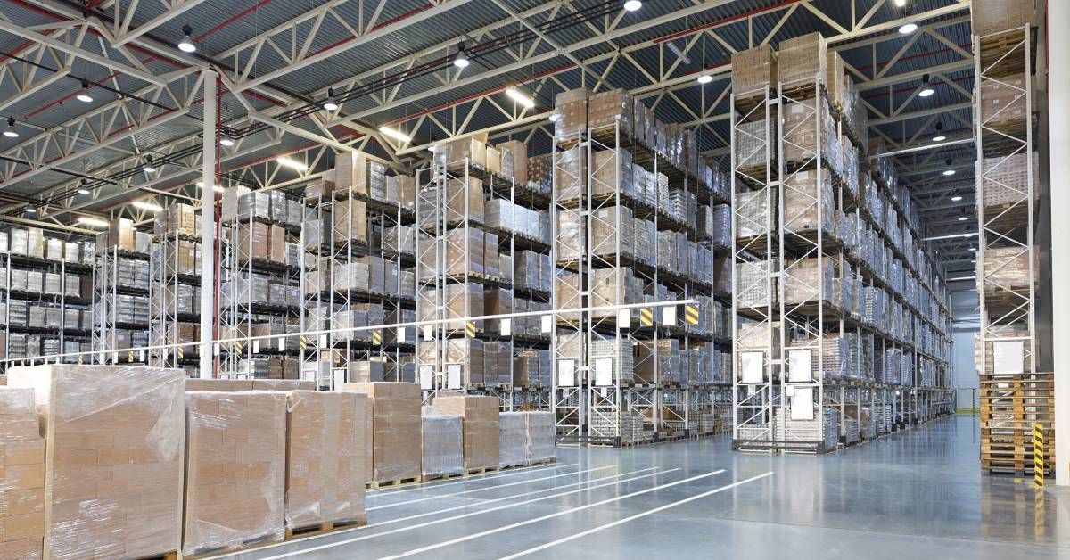 An expansive warehouse of a distribution center that features floor-to-ceiling pallet rack shelving systems with boxes.