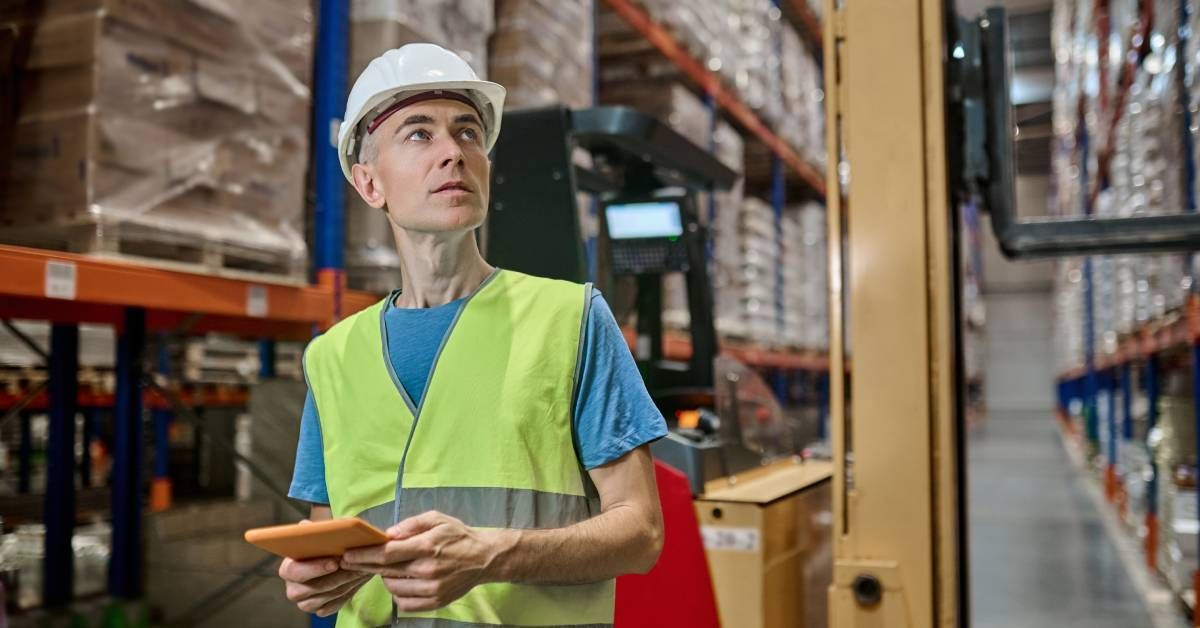 A warehouse manager conducting a rack inspection. He looks over the racking system while consulting his tablet.