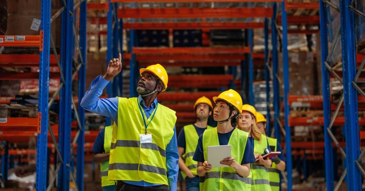 A group of warehouse workers dressed in reflective vests and hard hats inspecting racking systems.