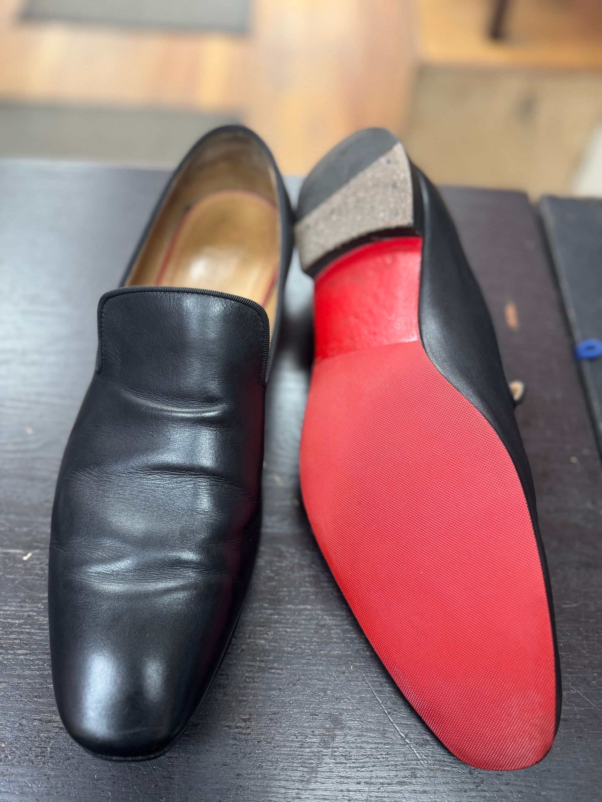 A pair of black leather loafers, one shown from above and the other flipped to display a signature red lacquered sole.