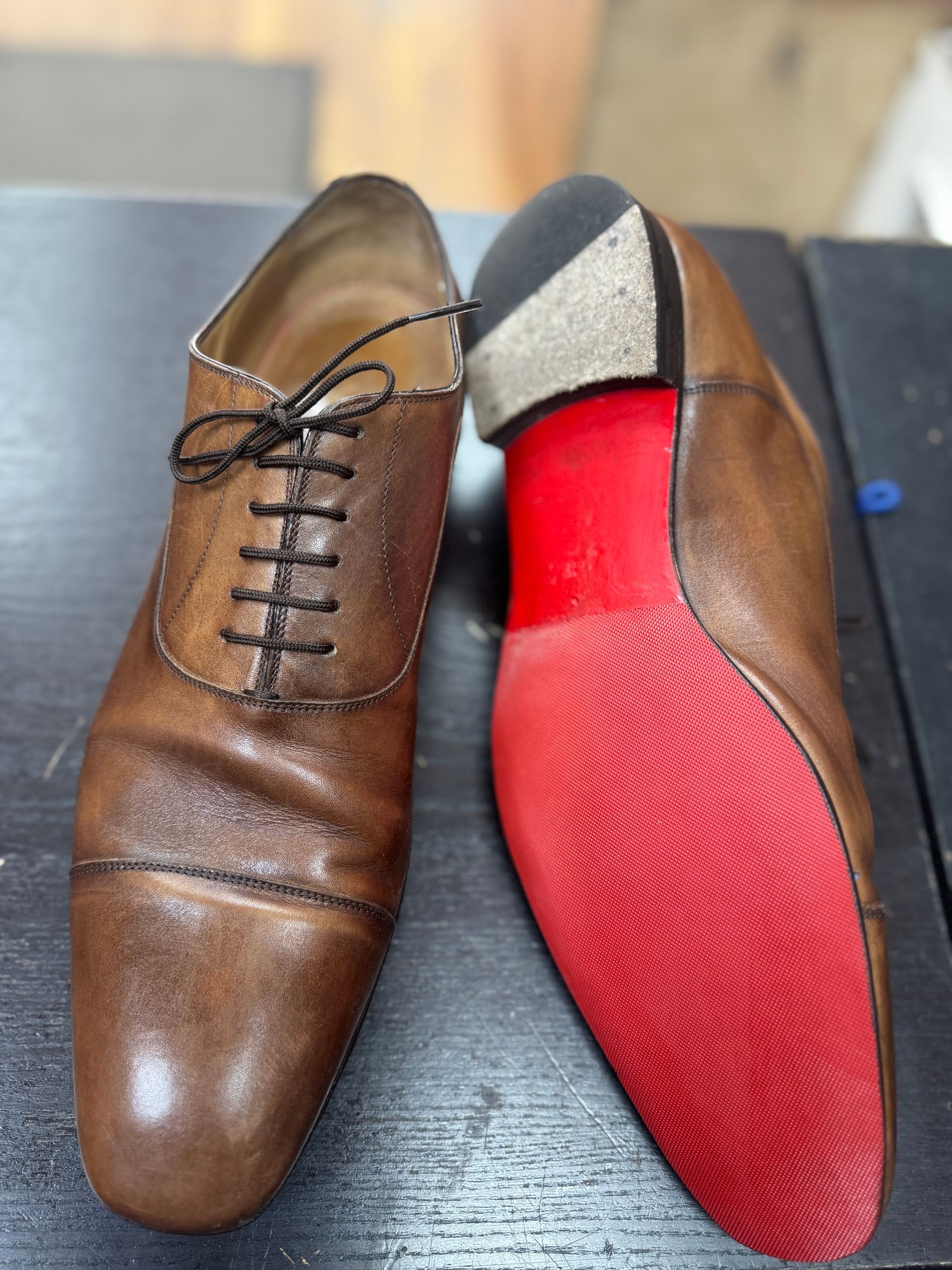 A pair of brown leather oxford dress shoes, one showing the top and the other displaying a distinctive bright red sole.