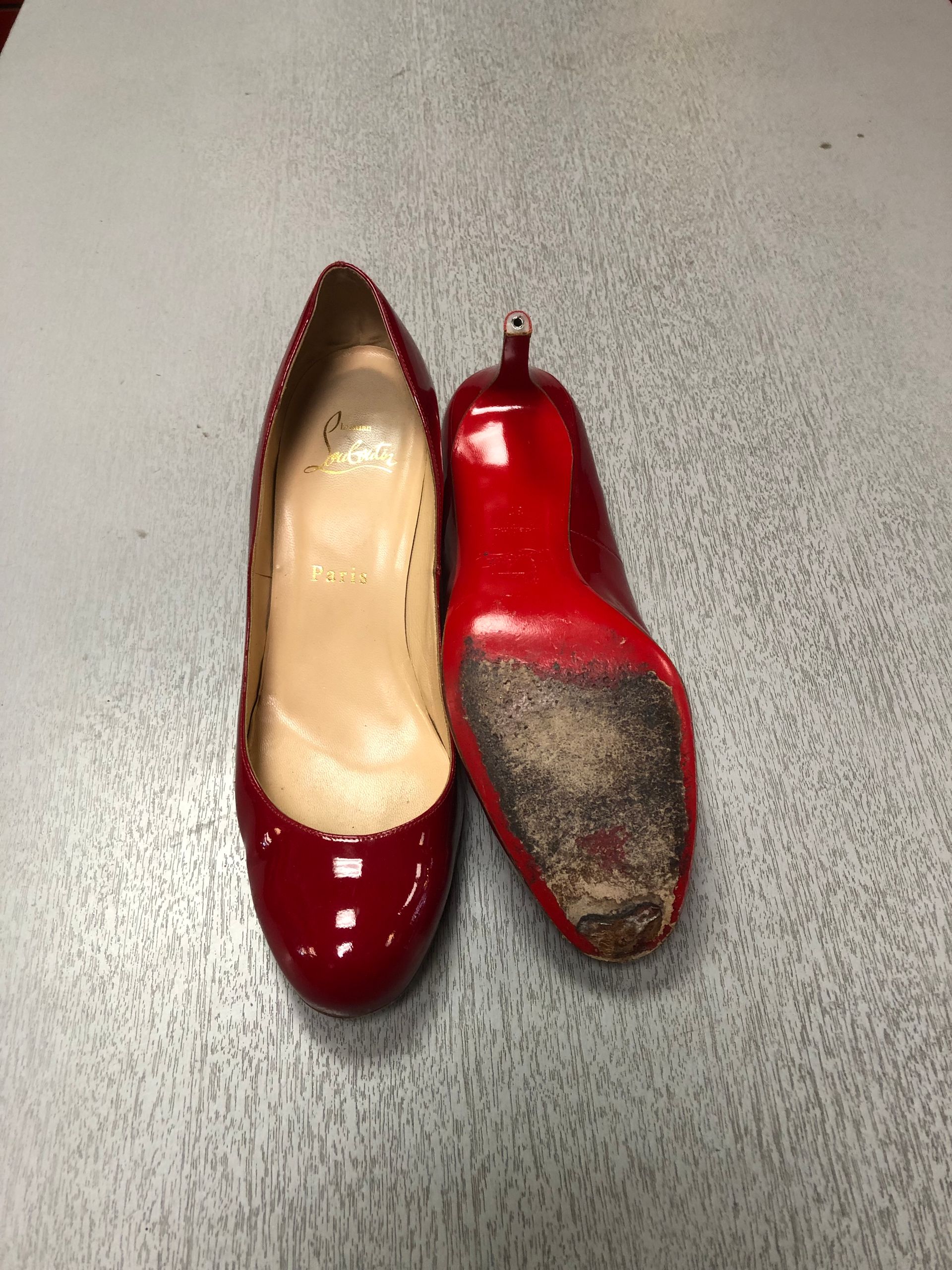A pair of red patent leather high-heeled pumps placed on a gray surface; one is shown upright, the other sole-up.