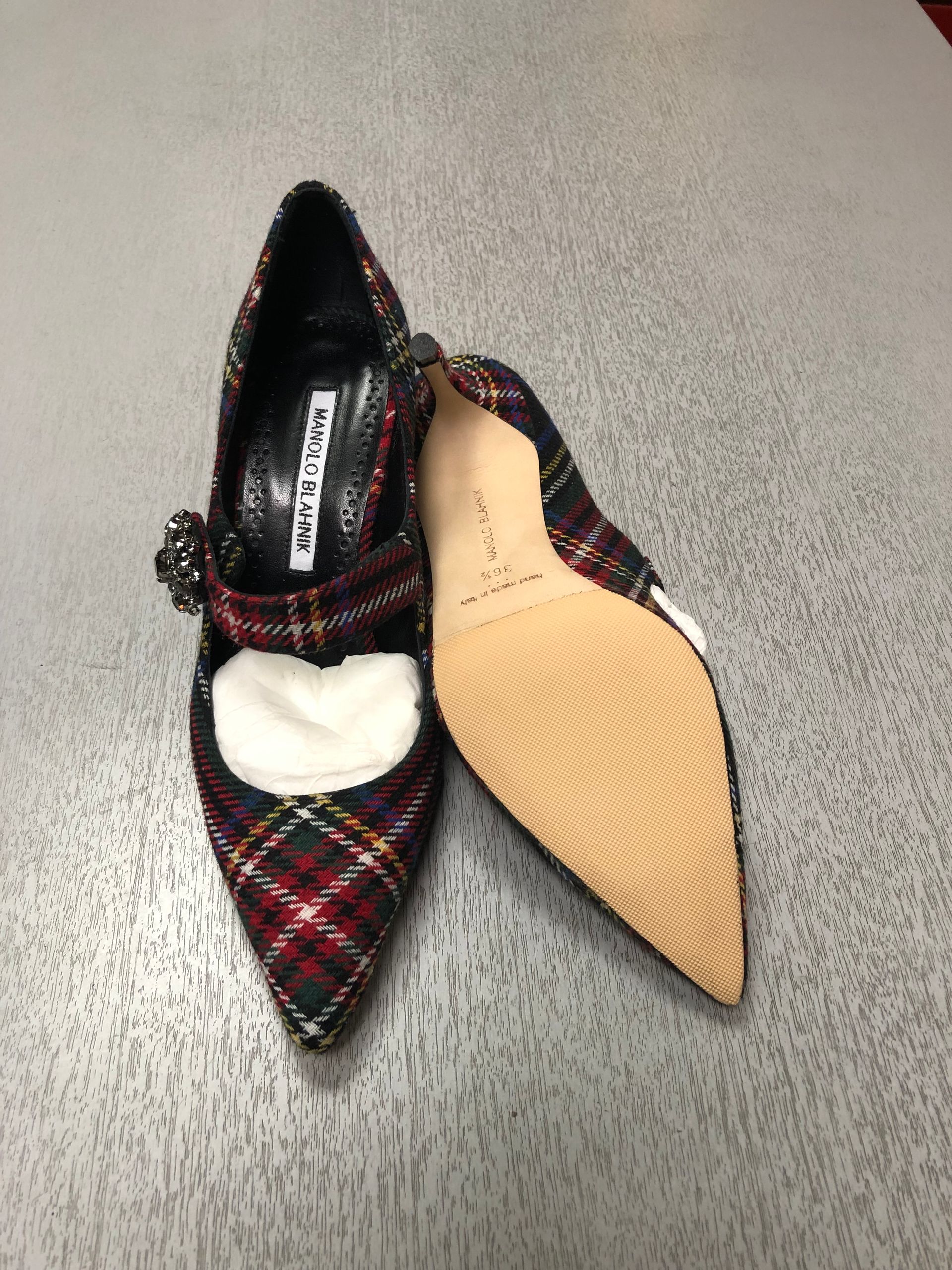 A pair of pointed-toe pumps in a red, green, and black plaid fabric, featuring a jeweled strap across the instep.