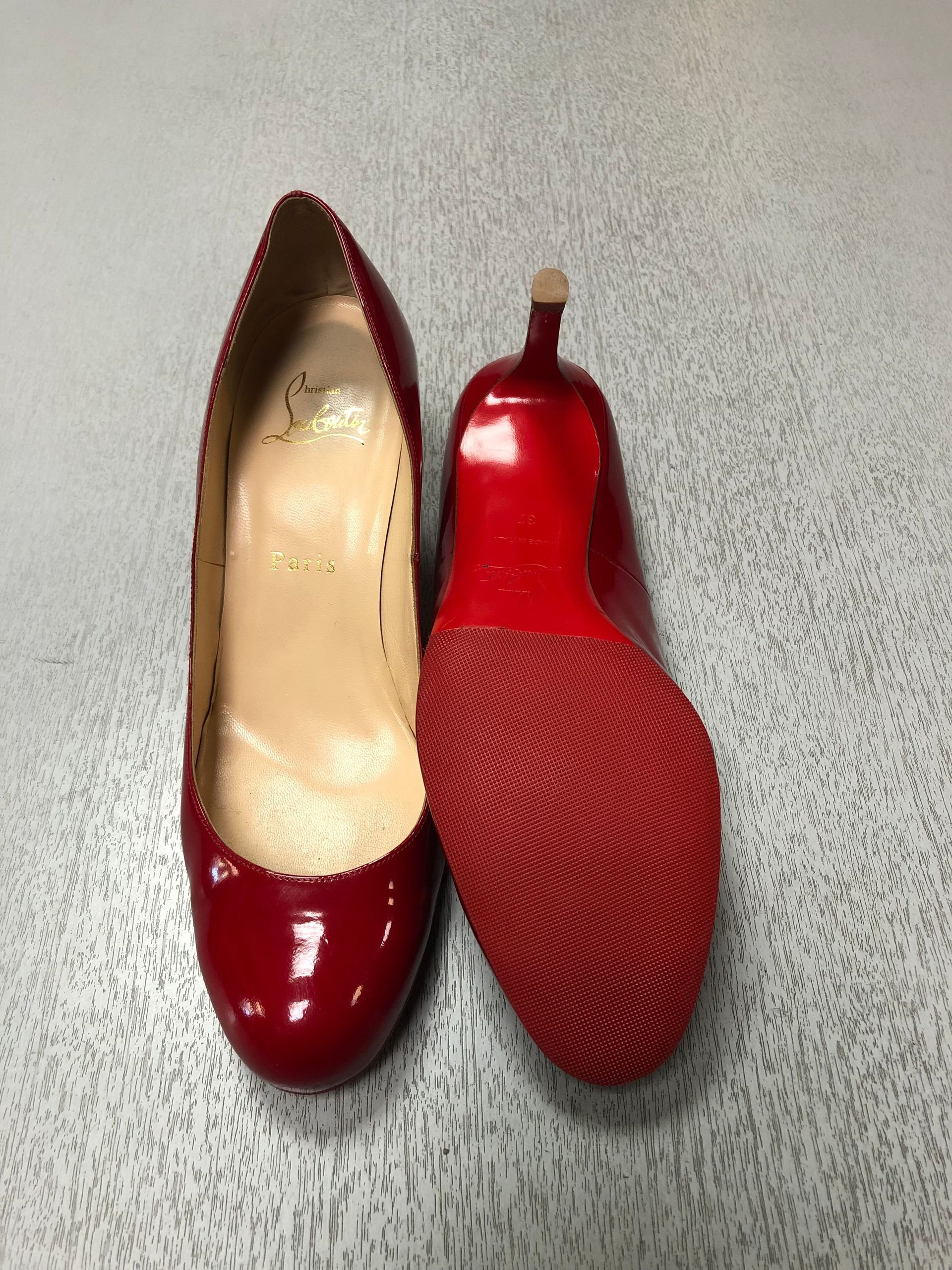 A pair of red patent leather high-heeled shoes, one displayed from the inside and the other showing the red sole.