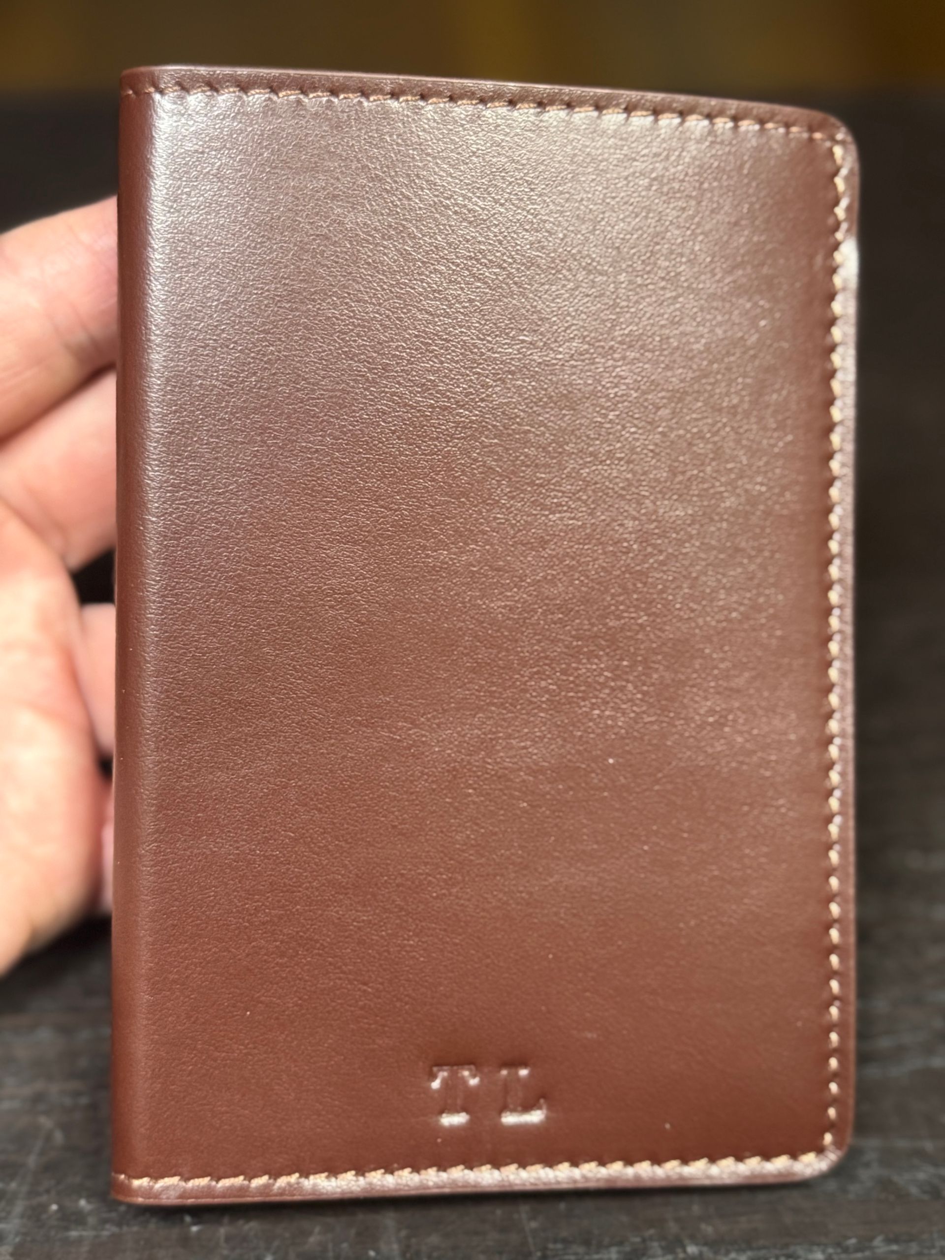 A person holds a smooth, dark brown leather wallet with embossed 