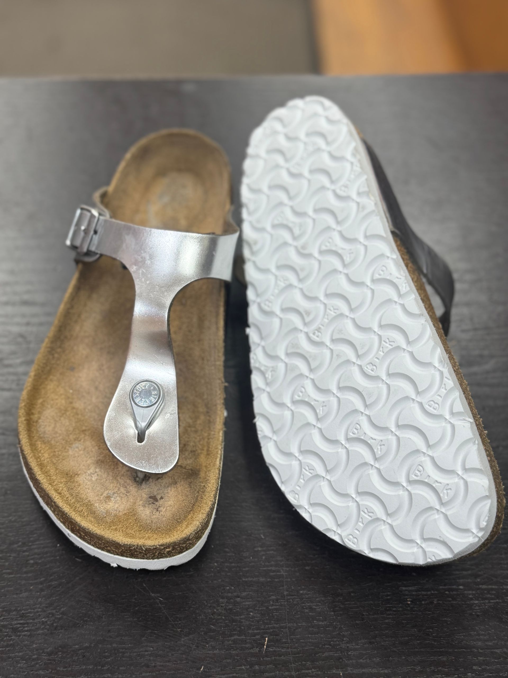 A pair of silver thong-style sandals: one showing the contoured footbed and the other showing the white patterned sole.