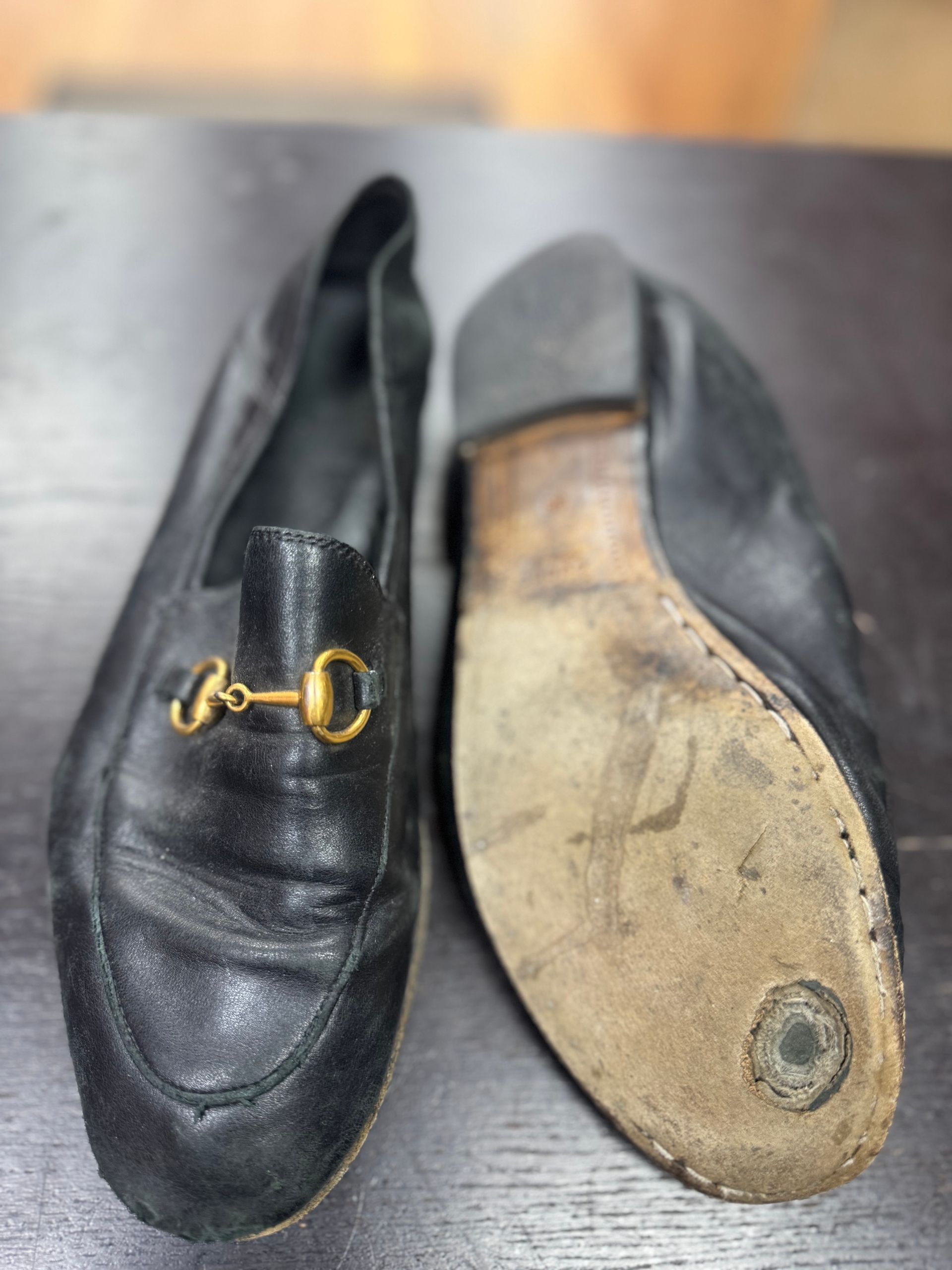 A pair of black leather Gucci loafers, one shown from the top with a gold horsebit detail, the other showing a worn sole.