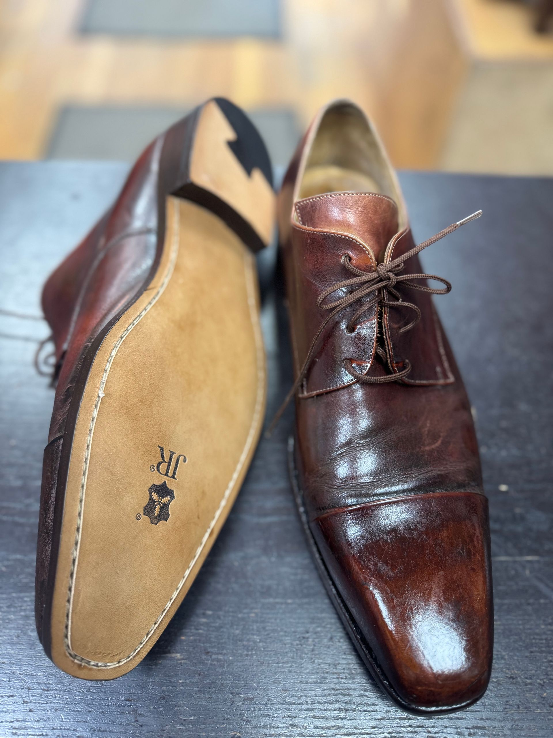 A pair of brown leather oxford dress shoes, one showing the stitched leather sole with a JR brand mark.