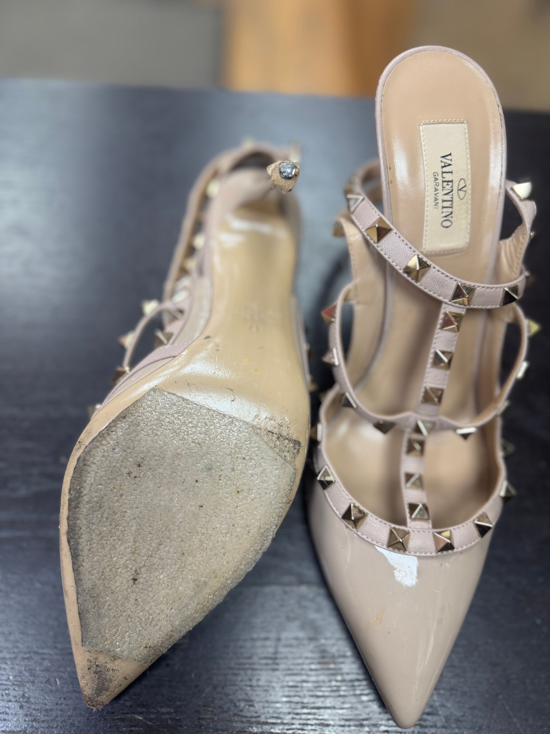A pair of beige Valentino Rockstud stiletto heels resting on a dark surface, showing both the sole and top view.