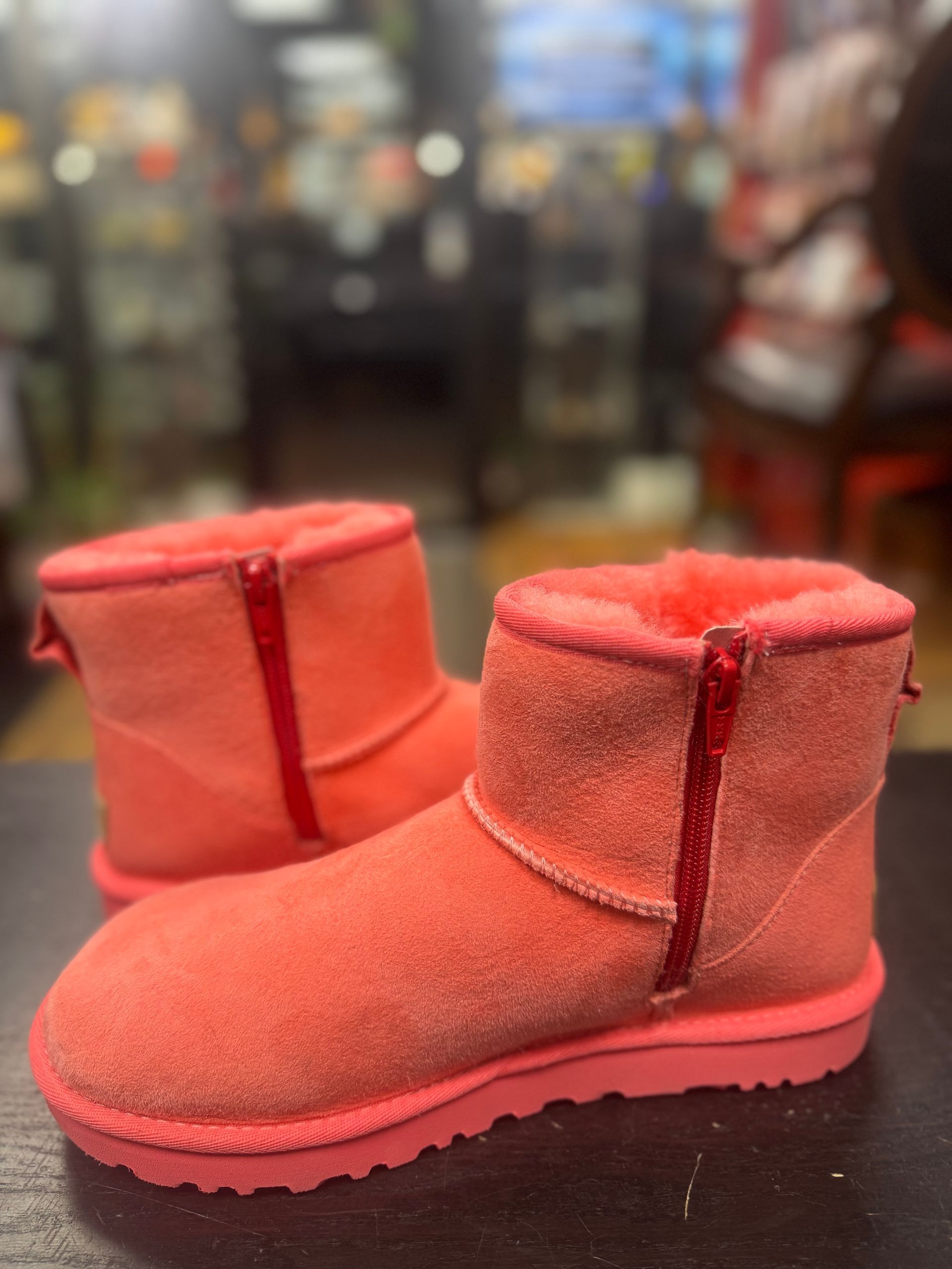 A pair of vibrant coral-colored suede ankle boots with a prominent side zipper, resting on a dark surface.