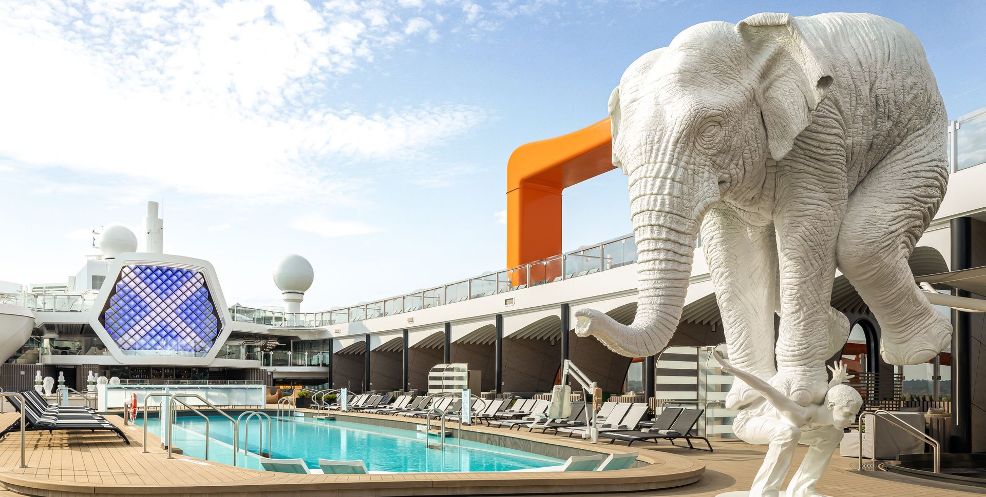 Cruise ship deck with pool, orange arch, lounge chairs, and partial view of the sea.