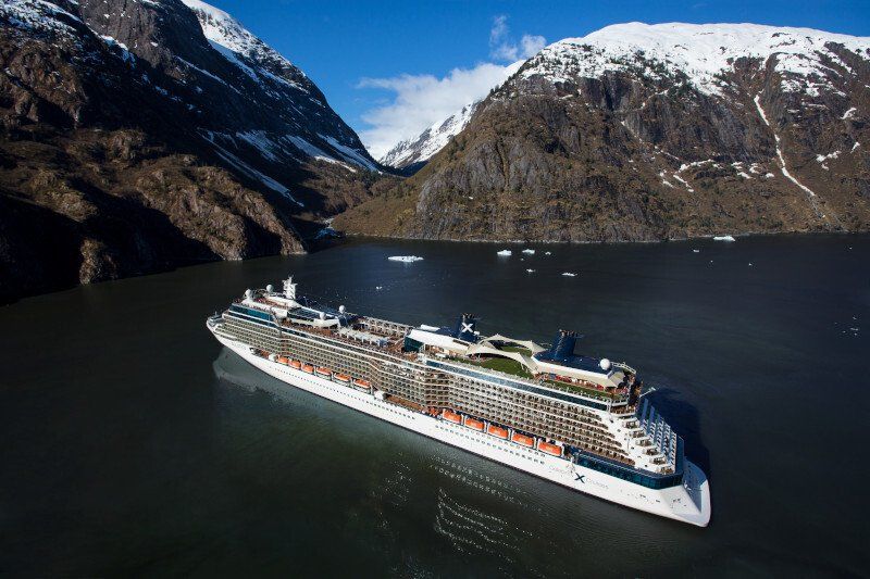 A large cruise ship is floating in a body of water surrounded by snow covered mountains.