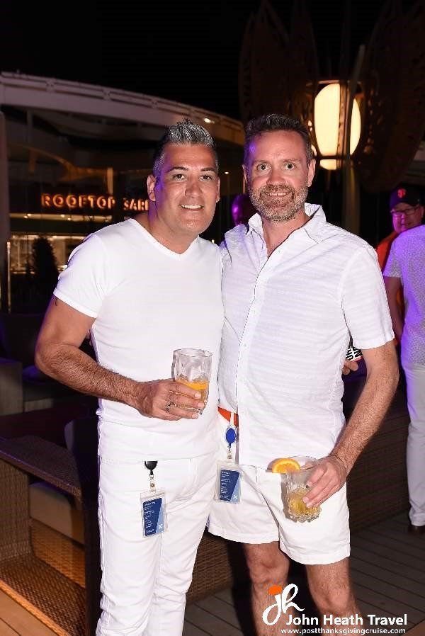 Two men in white shirts and shorts are standing next to each other holding drinks.