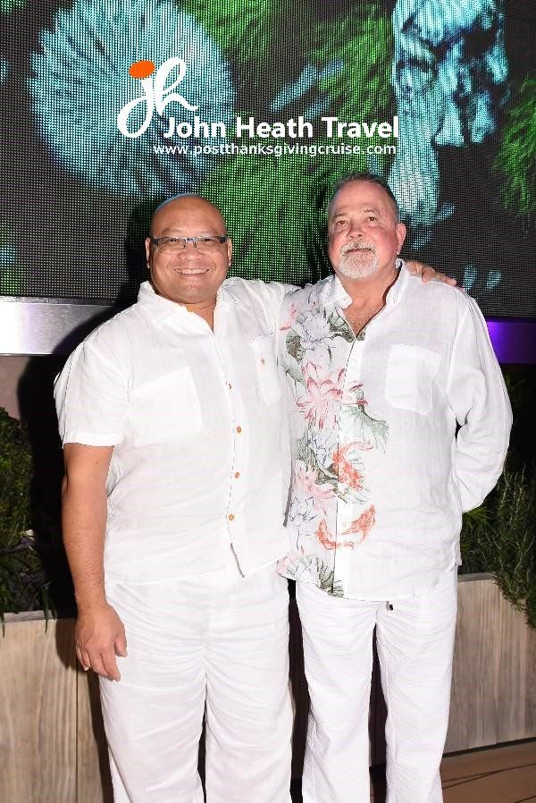 Two men are standing next to each other in front of a large screen.